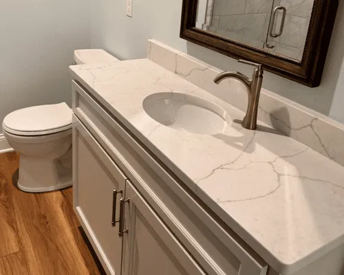 Bathroom vanity with a white countertop and marble-style veining, a metal faucet, cabinet doors, and a toilet nearby.