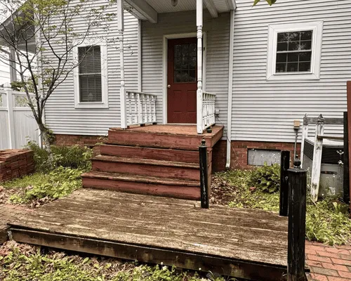 A front porch and wooden steps leading to a red door on a house with light gray siding.