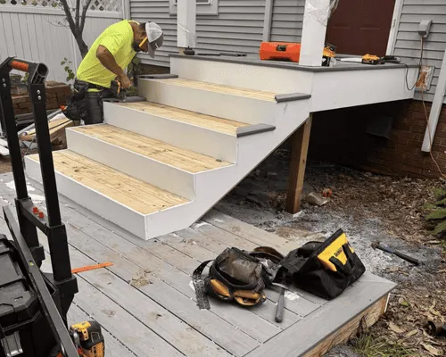 A person in a neon yellow shirt works on installing wooden steps for an outdoor deck.