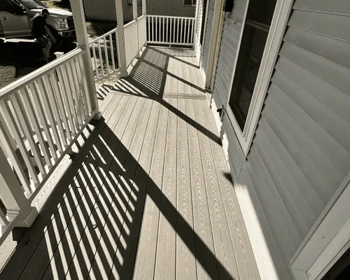 A grey wooden porch with white railings, casting long, sharp shadows under bright sunlight next to white siding.