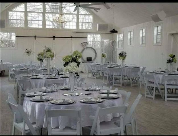 Wedding reception hall with white tables, chairs, and floral centerpieces. Bright, open space.