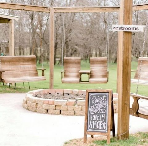A sign that says restrooms is next to a fire pit and swings.