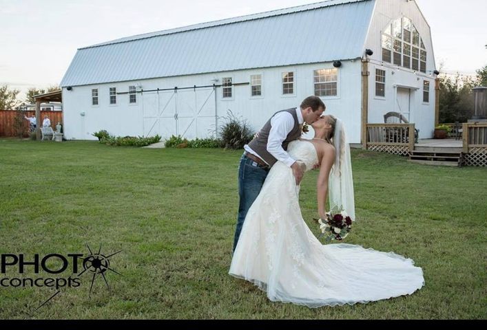 Wedding couple kissing in front of a white barn on a green lawn.