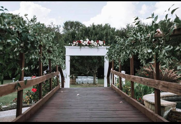 Wooden bridge leading to a wedding ceremony setup with white arch decorated with flowers.