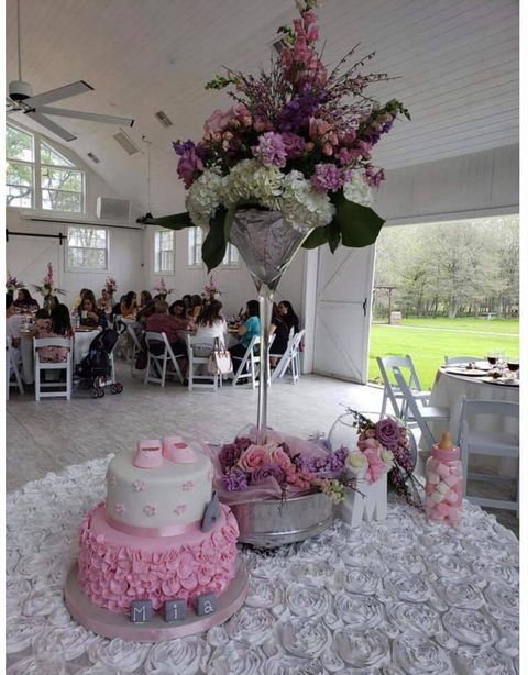 Baby shower table setting with cake, flowers, and guests in a white event space.