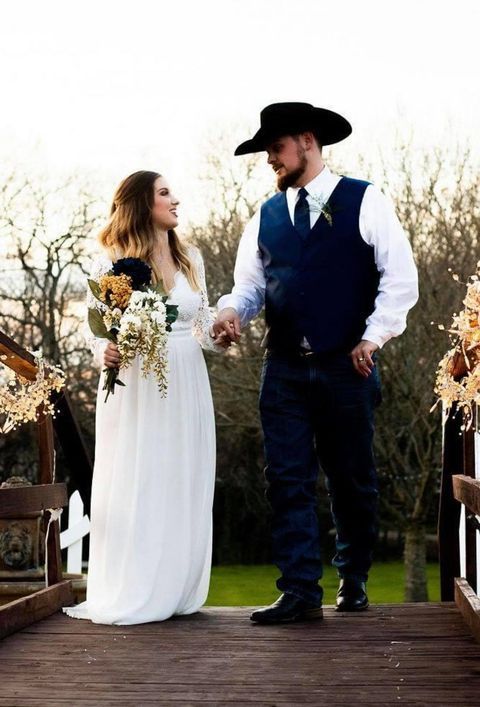 Couple in wedding attire holding hands on a wooden bridge, looking at each other.