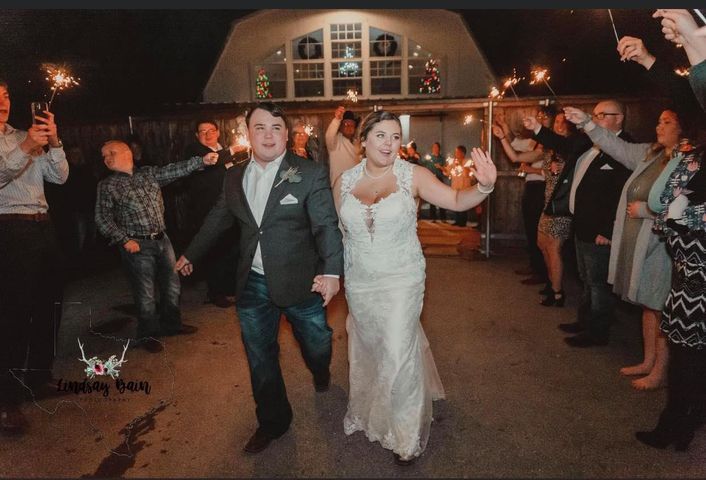 Newlyweds exit a building, holding hands, flanked by guests waving sparklers at night.