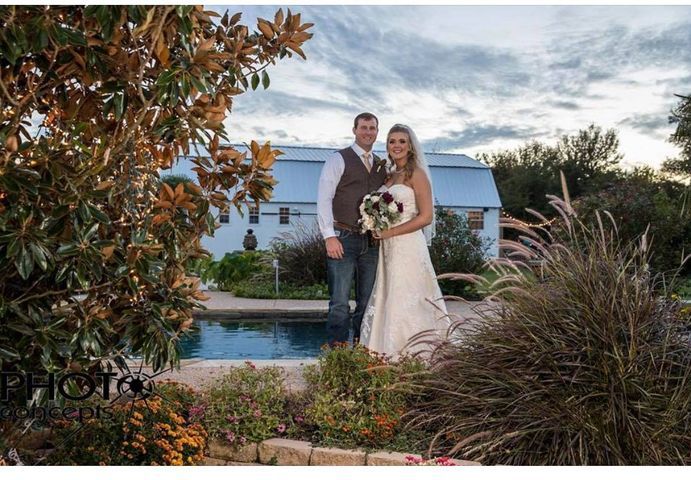 Couple posing by a pool in front of a white building, surrounded by plants and a cloudy sky.