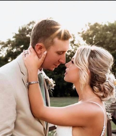Bride and groom face each other, bathed in sunlight. She caresses his face. Outdoor wedding.