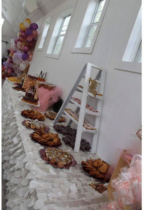 A dessert table with cakes, cookies, and other treats, decorated with balloons and a white tablecloth.