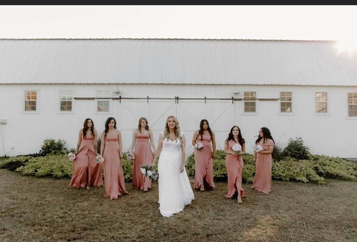 Bride in white dress with bridesmaids in pink gowns posing in front of white barn.