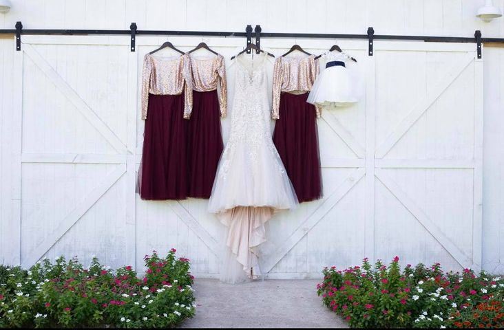 Wedding dresses and bridesmaid dresses hanging on a white barn door, with flowerbeds below.