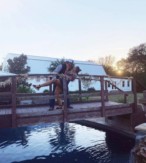 A man is holding a woman on a bridge over a body of water.