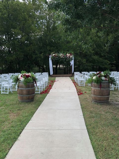A concrete walkway leading to a wedding ceremony with barrels filled with flowers.