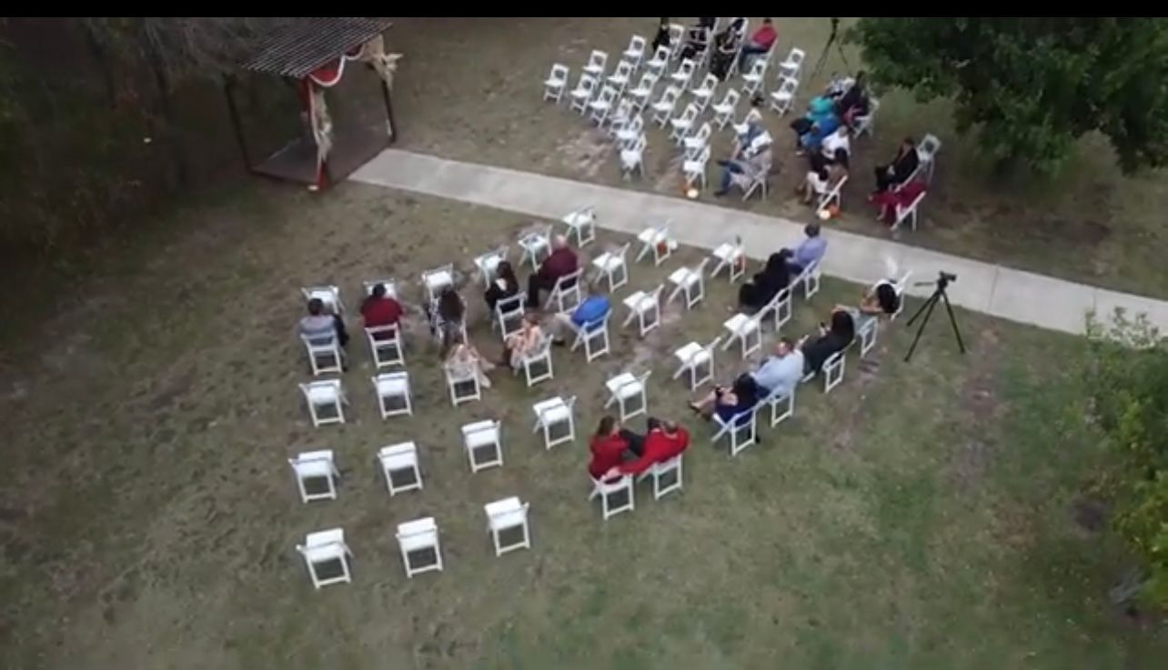 Outdoor wedding ceremony, rows of white chairs, guests seated, path to altar, green lawn.