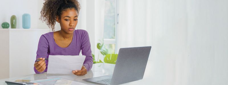 A woman is sitting at a table with a laptop and a piece of paper.