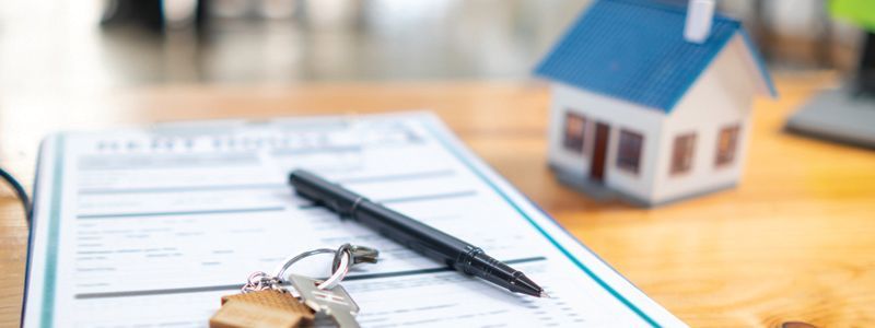 a pen, keys, and a model house are on a piece of paper on a table.