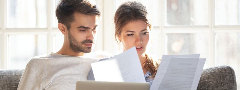 a man and a woman are sitting on a couch looking at papers.