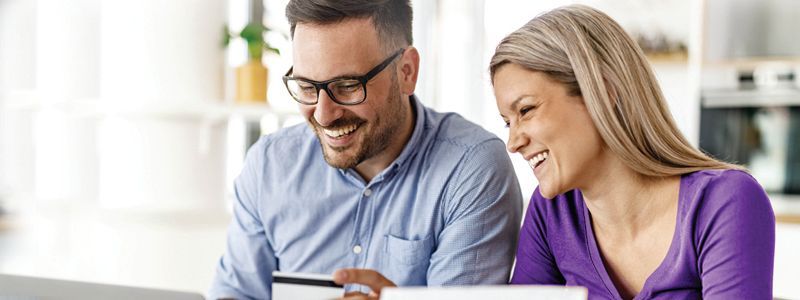 a man and a woman are sitting at a table looking at a laptop while holding a credit card.