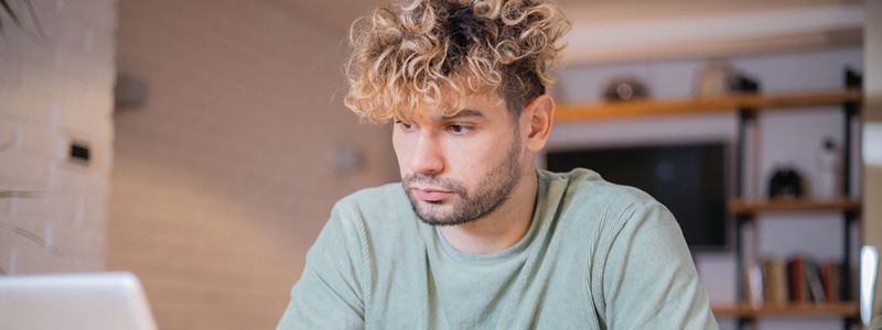 A man with curly hair is sitting in front of a laptop computer.