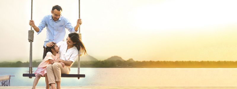 Two people and a child on a rope swing over a calm lake at sunset