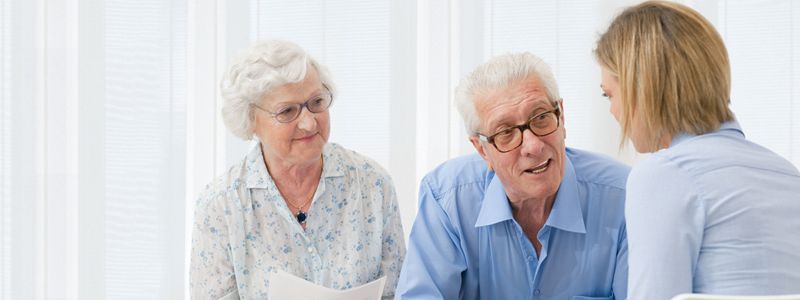 Elderly couple consults with a younger woman, discussing documents indoors.