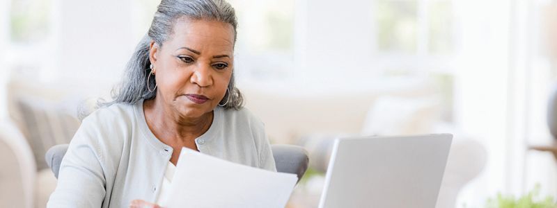 Woman with gray hair looking at documents and laptop. Indoors, natural light.