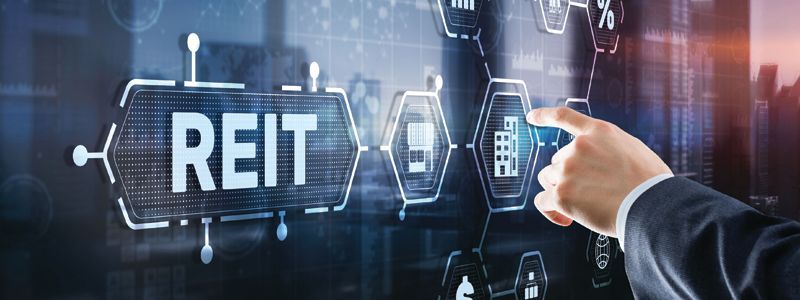 Hand in suit pointing at glowing REIT text on a digital finance interface
