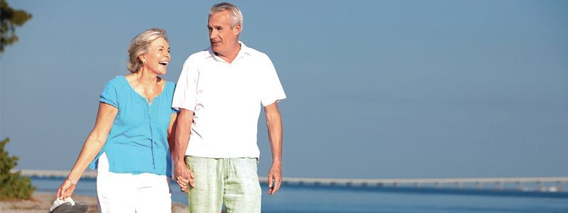Couple walking hand in hand along a beach under a clear blue sky