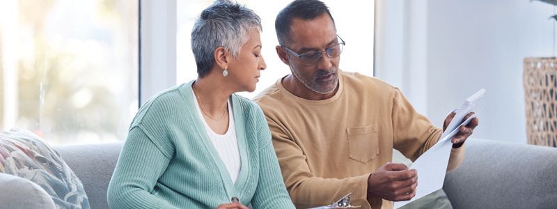 A man and a woman are sitting on a couch looking at a piece of paper.