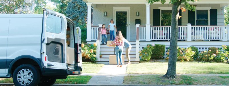 People standing at a house entrance beside a white van parked on the street