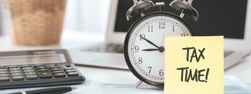 An alarm clock is sitting on a desk next to a calculator and a sticky note that says