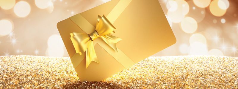 Golden gift with a ribbon bow on a shimmering surface with bokeh lights in the background.
