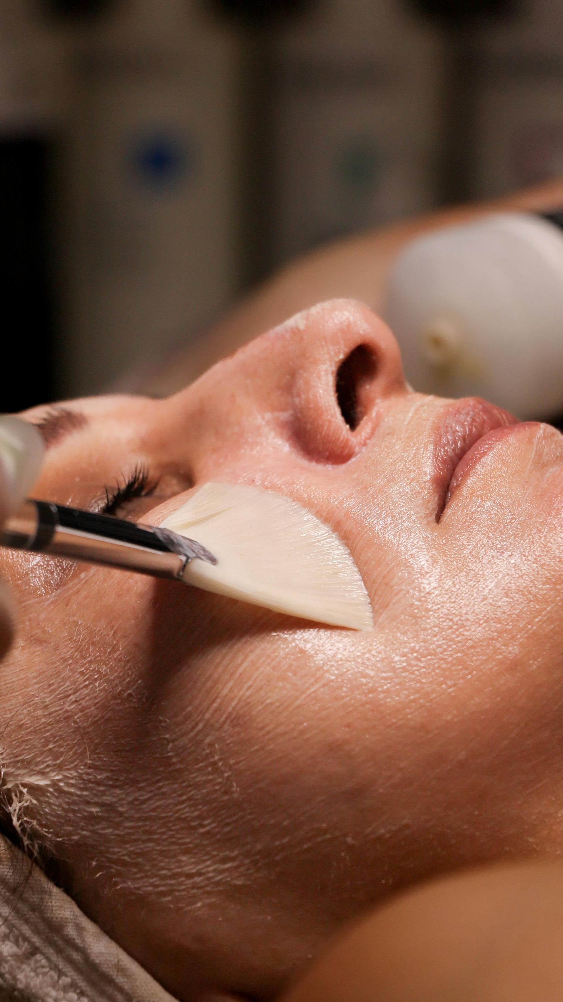 Facial treatment with a brush applying cream to a person’s cheek in a spa setting