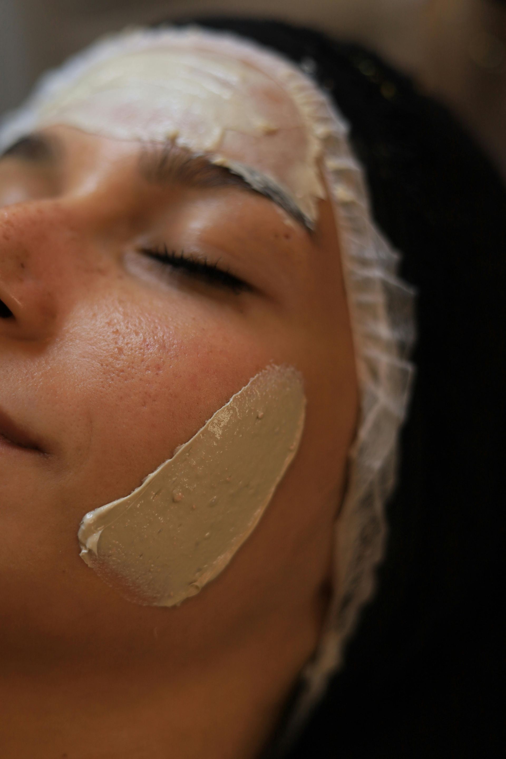 Person lying down with facial mask cream applied to forehead and cheek, eyes closed.