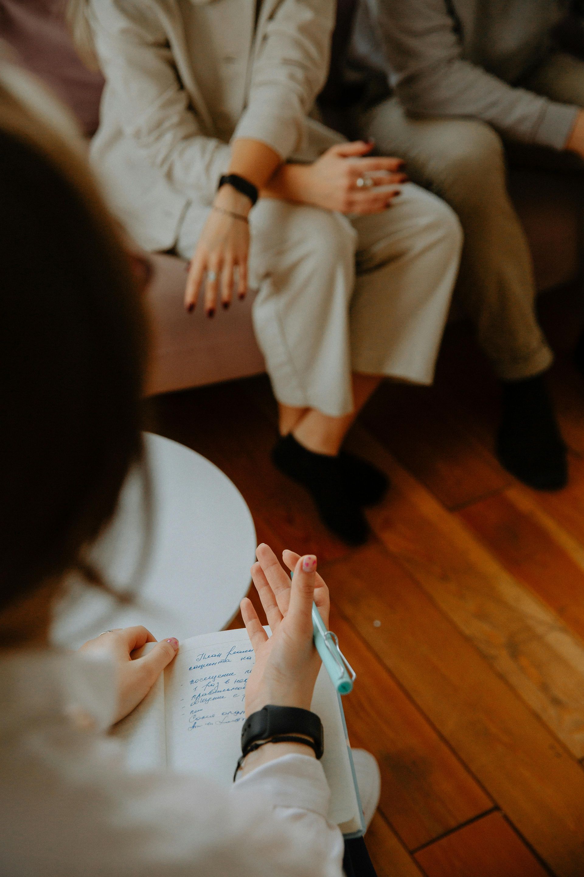 People seated in a circle, hands clasped, during a group discussion on a wooden floor