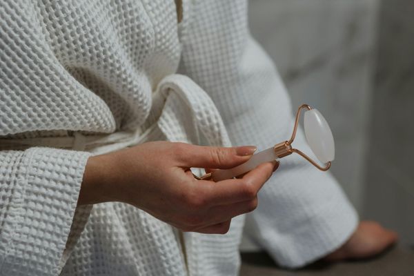 Hand holding a gold-rimmed eyeglass in a white robe near a bed