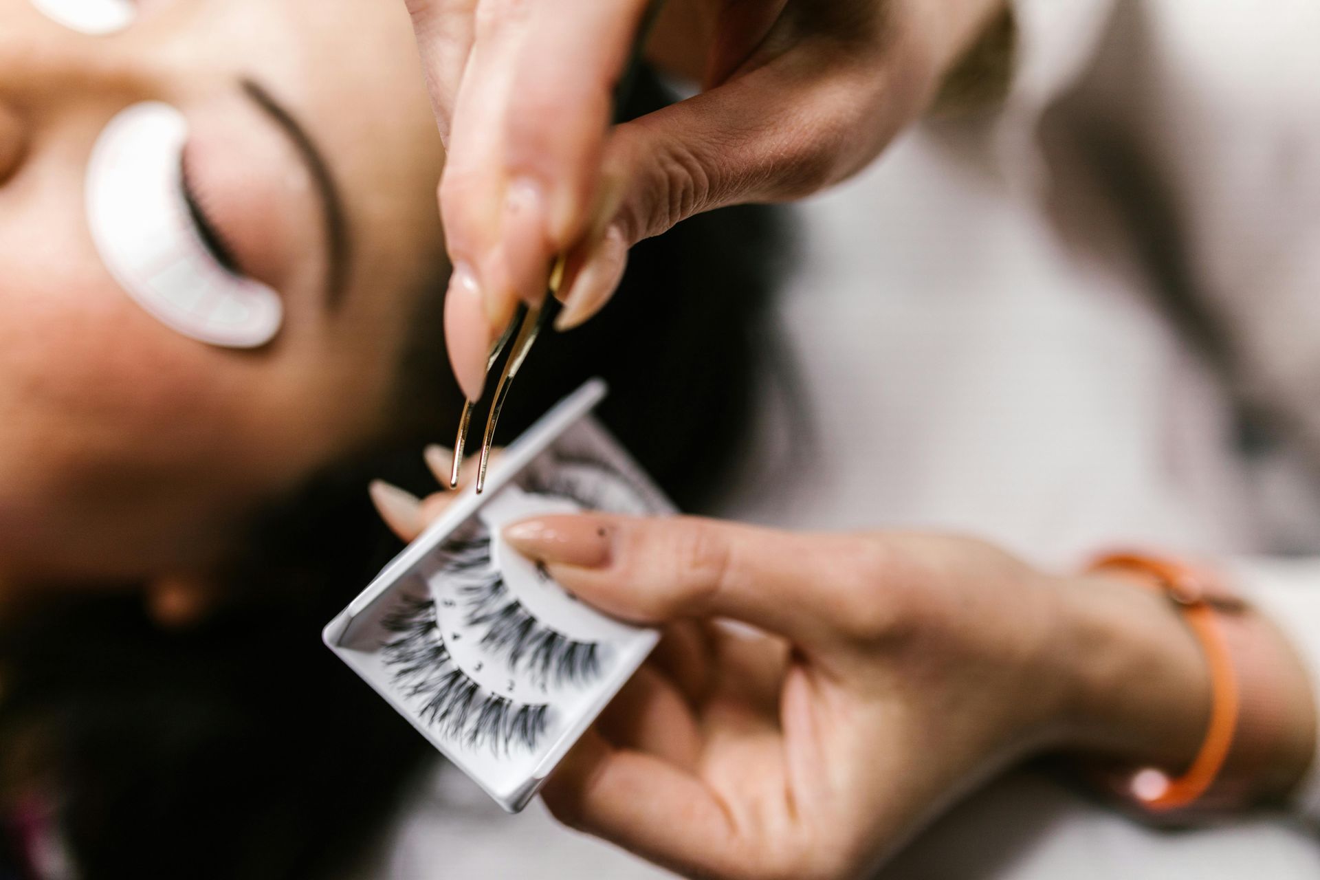 Close-up of eyelash extensions being applied with tweezers on a client’s closed eye.