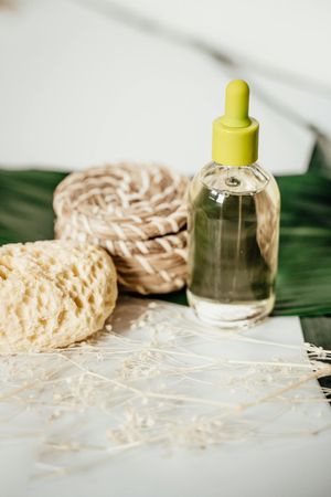 Glass bottle with yellow dropper beside woven soap pads on a light marble surface