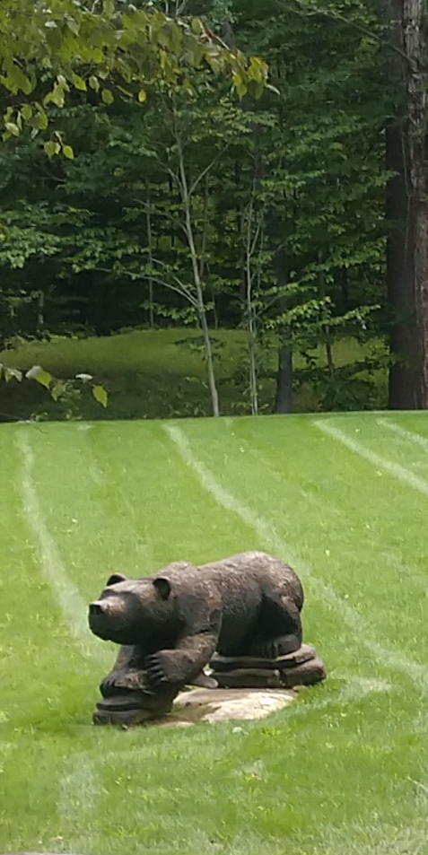 A statue of a bear laying on a log in a grassy field.