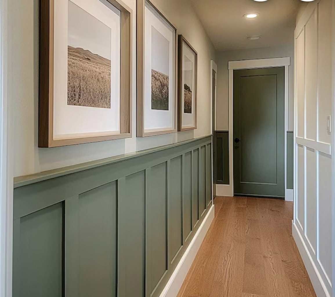 Hallway with olive-green wainscoting and door, three framed landscape prints, and wood flooring.