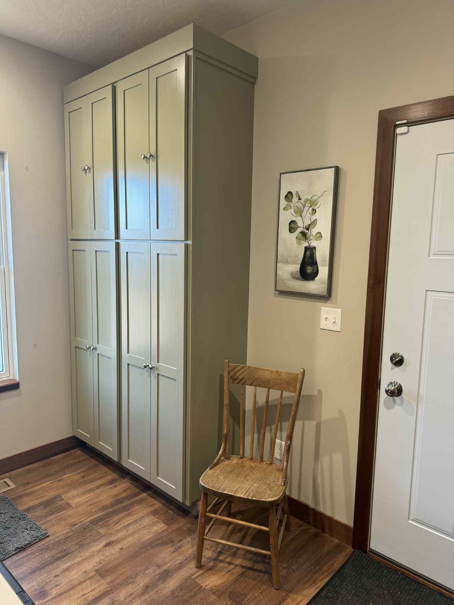 Tall, light green cabinets next to a wooden chair, artwork, and a front door.