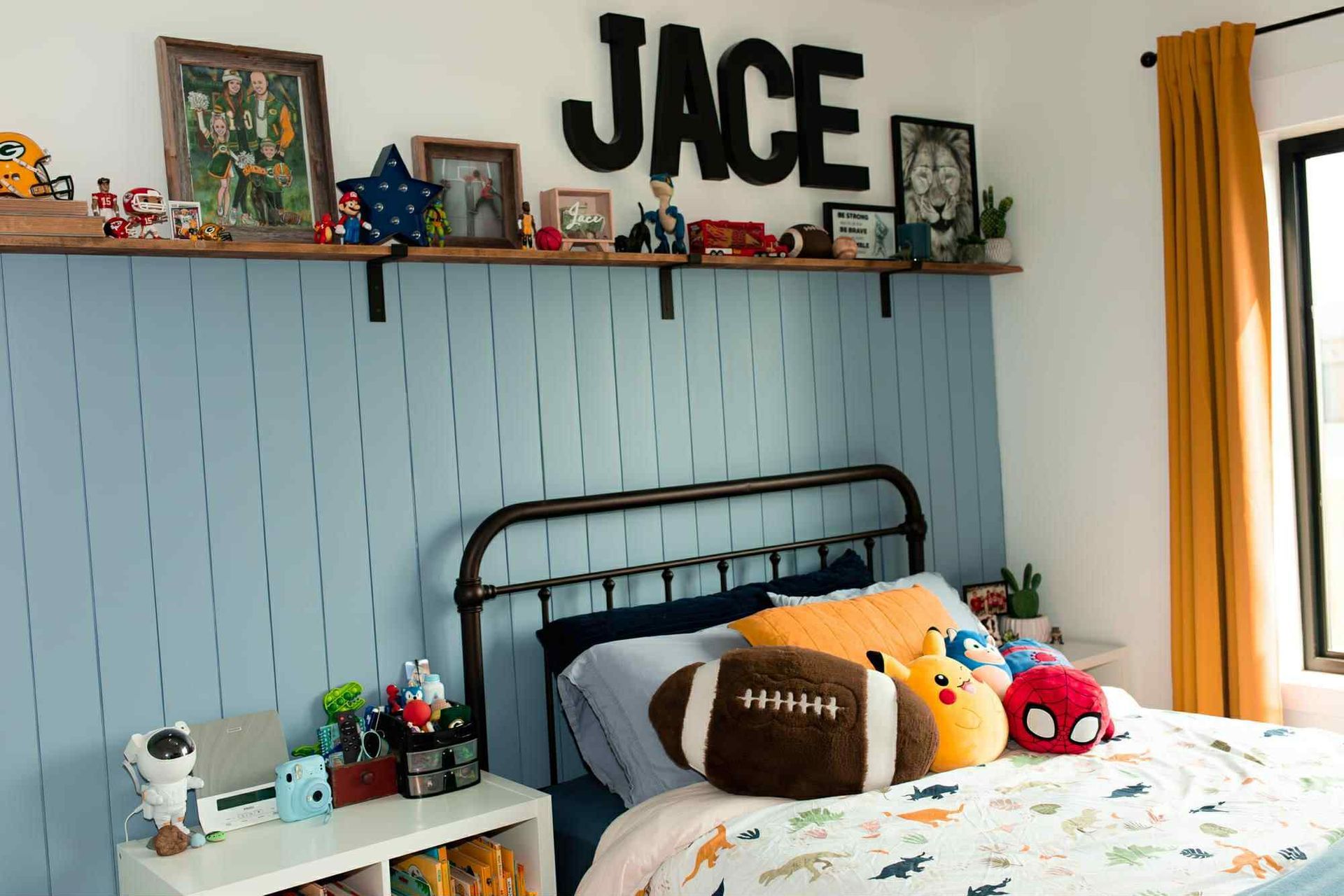 Bedroom with blue paneling, black bed frame, and a shelf with toys and JACE letters.