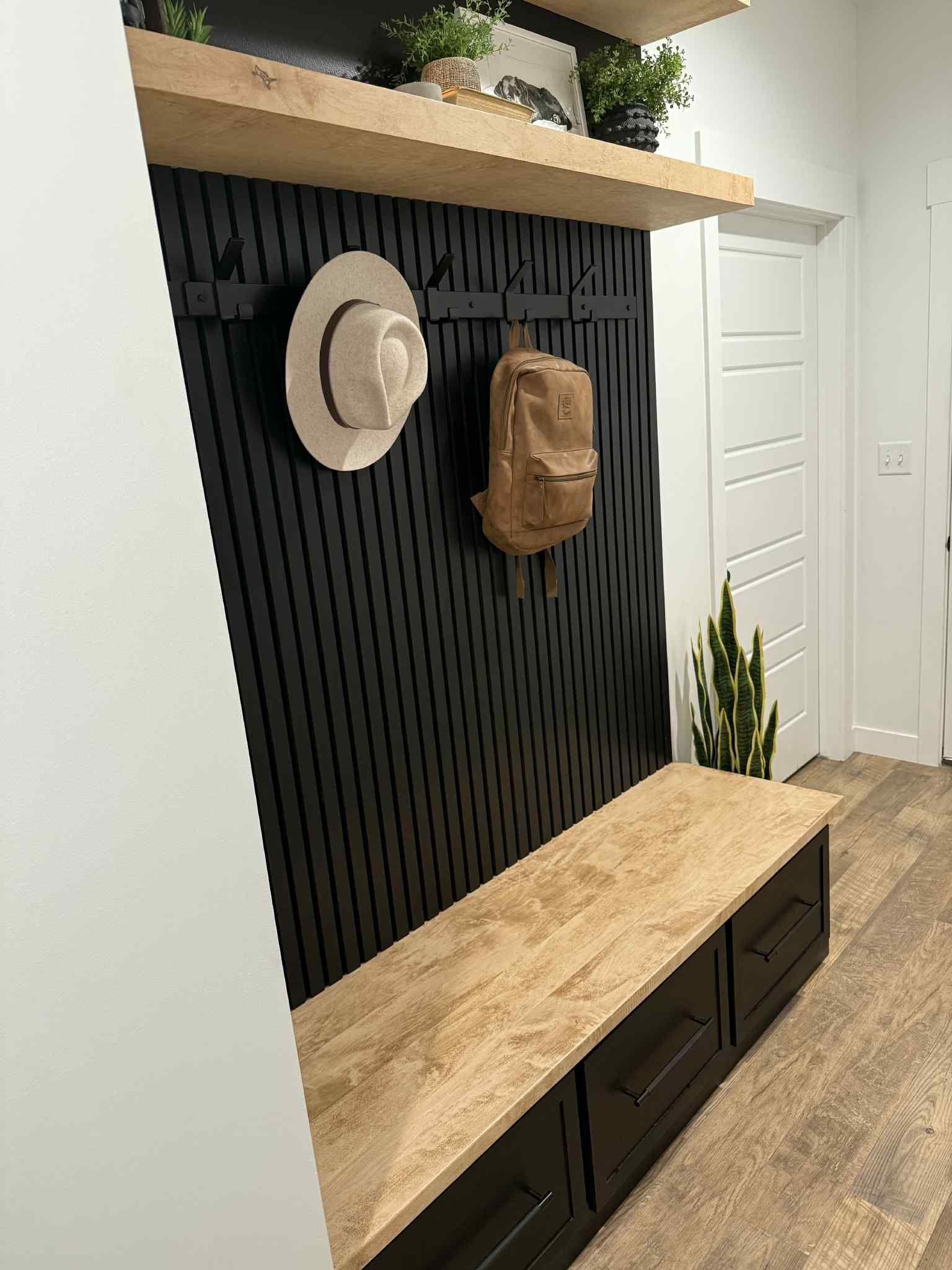 Hallway with black vertical slat wall, wood bench with drawers, shelves, hats, and a backpack.