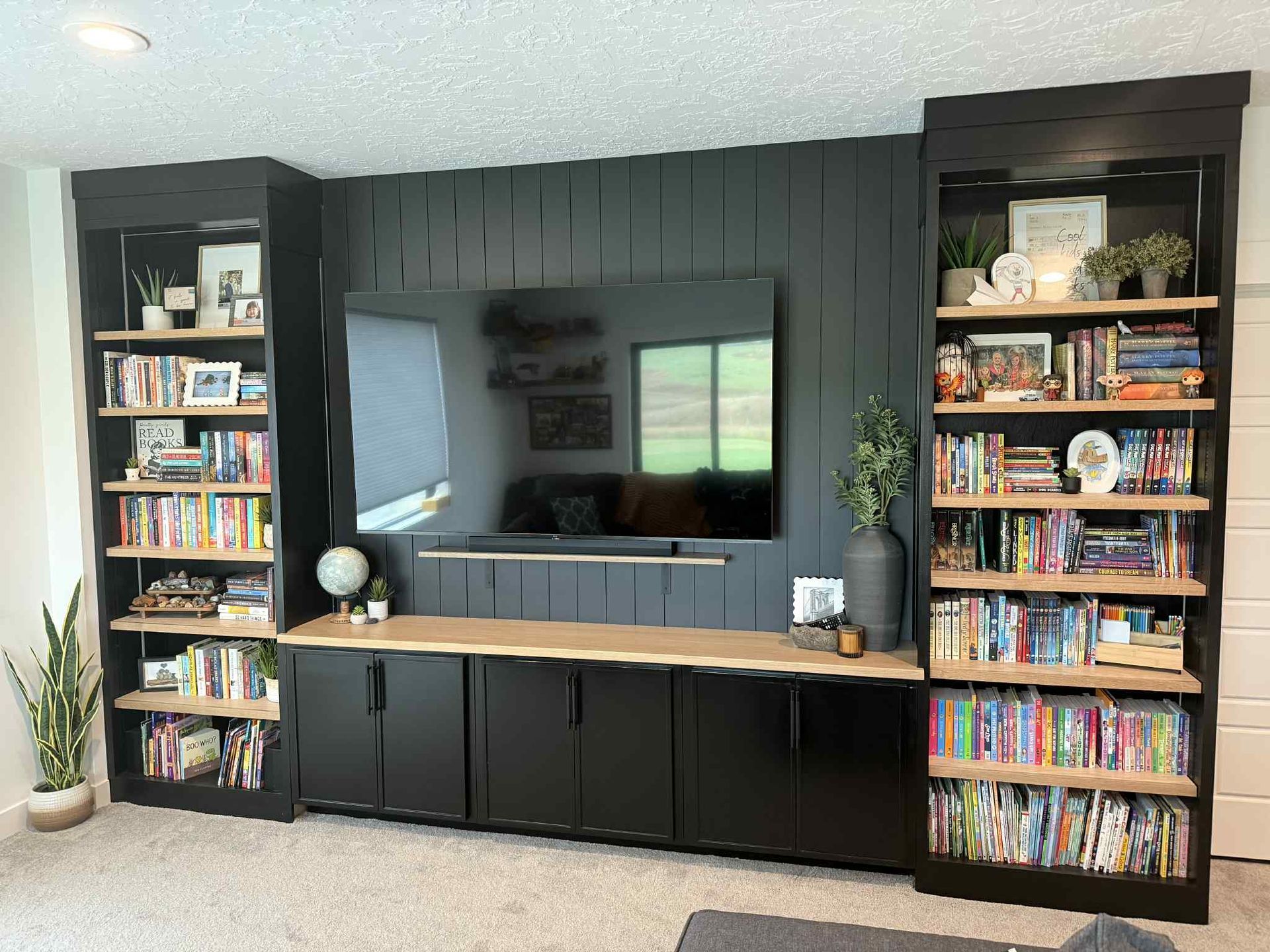 Built-in black entertainment center with a TV, shelving, cabinets, and light wood counter.