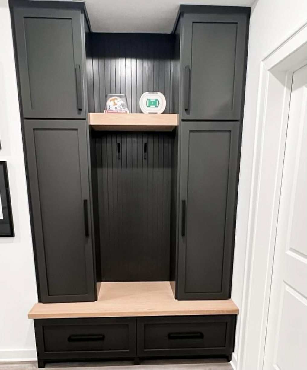 Black built-in entryway storage with cabinets, bench, drawers, and beadboard back.