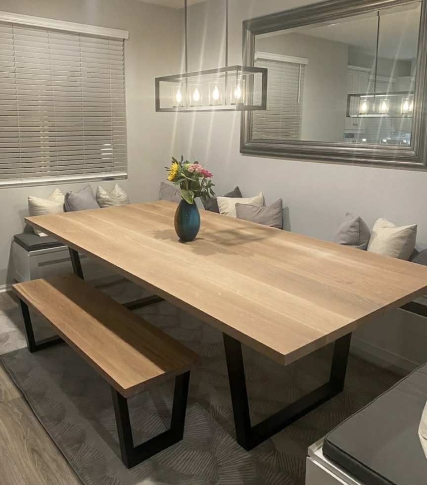 Dining room with a wooden table, bench, and built-in cushioned seating; gray walls and a large mirror.