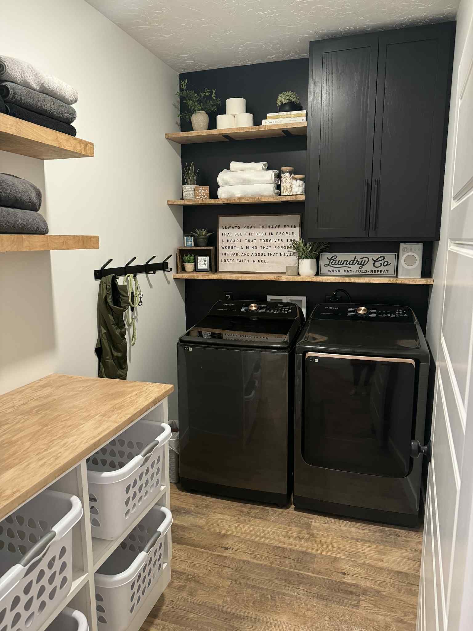 Laundry room with black appliances, black cabinets, and wooden shelves; white walls.