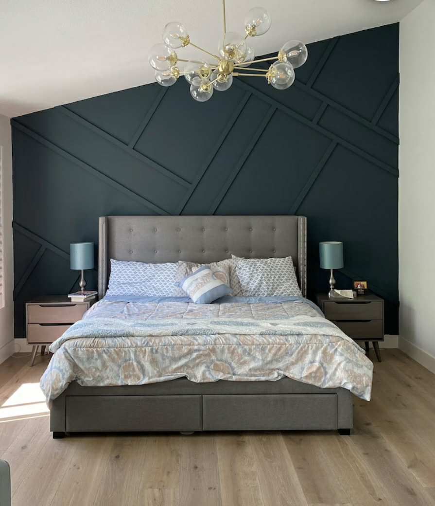 Bedroom with a geometric navy accent wall, gray bed, and modern light fixture.