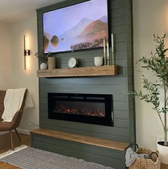 A modern fireplace setup with a mounted TV, olive green paneling, and a wooden bench.